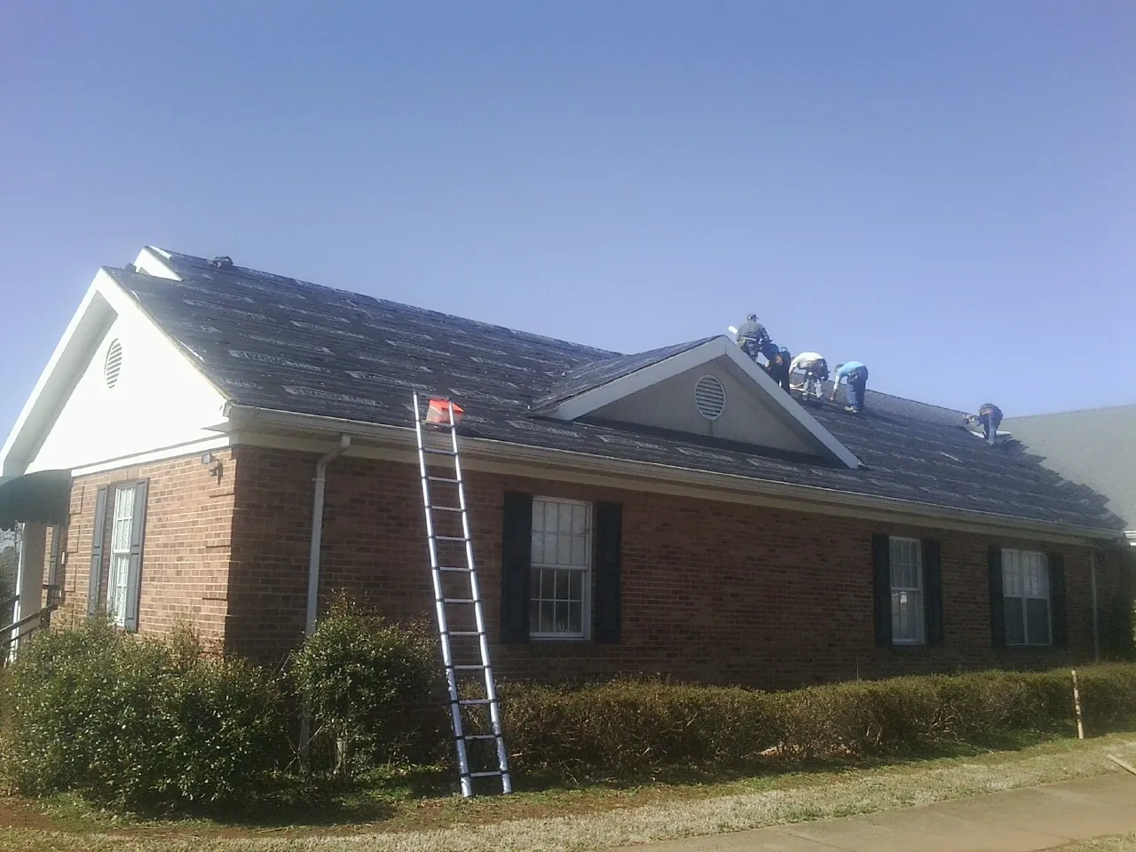 Crew tearing shingles off a brick ranch roof with a ladder set — Metal Roof Repair work by our crew in Beale Afb