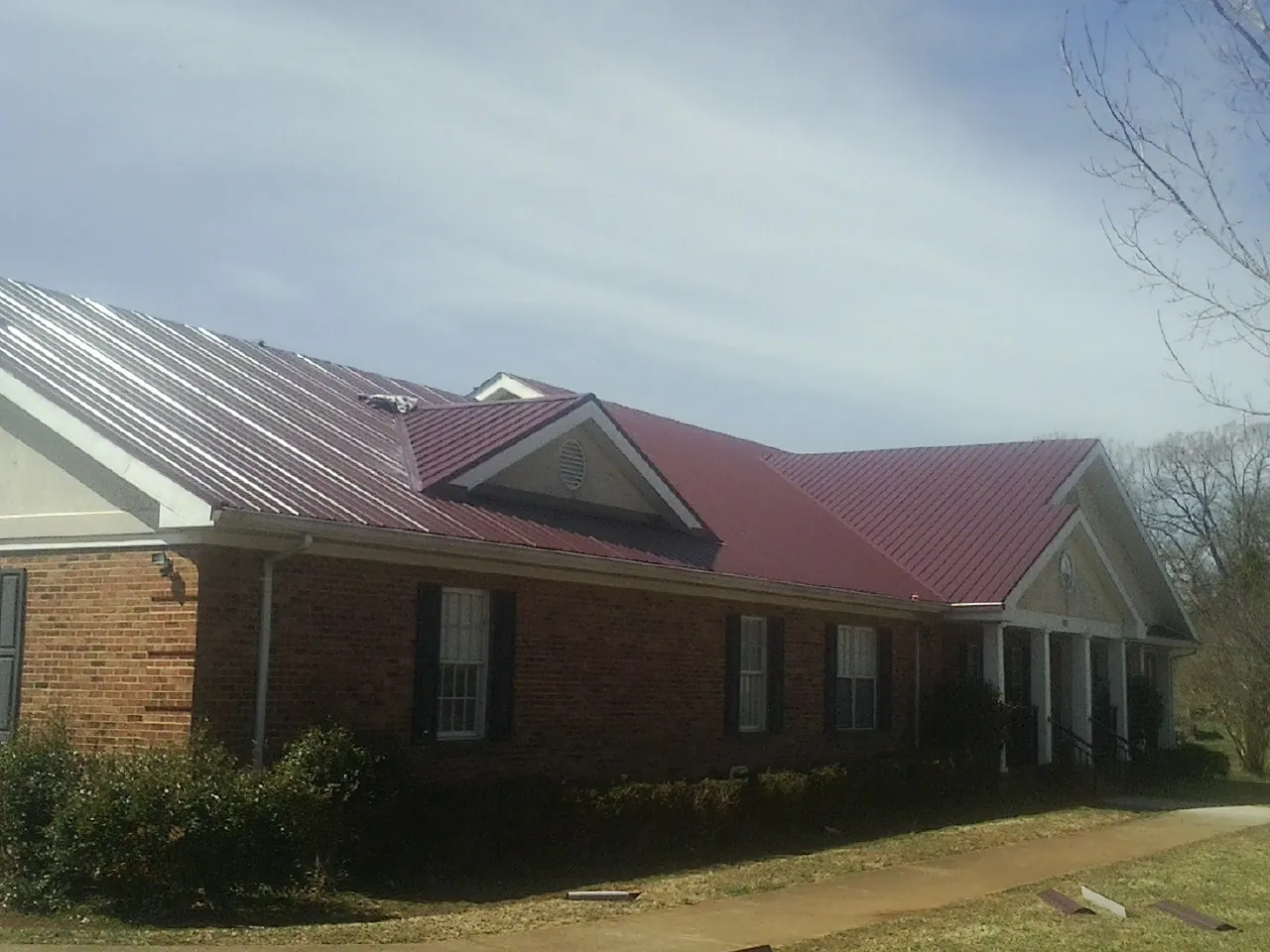 Red metal roof with gabled entries on a long brick building, from a Hail Damage Roof Repair job in Beale Afb