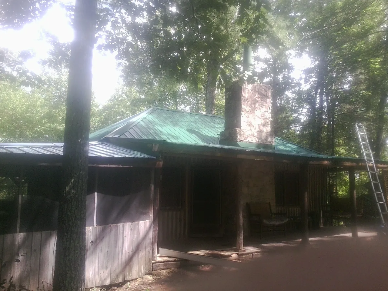 Green metal roof and stone chimney above a log cabin porch in Beale Afb