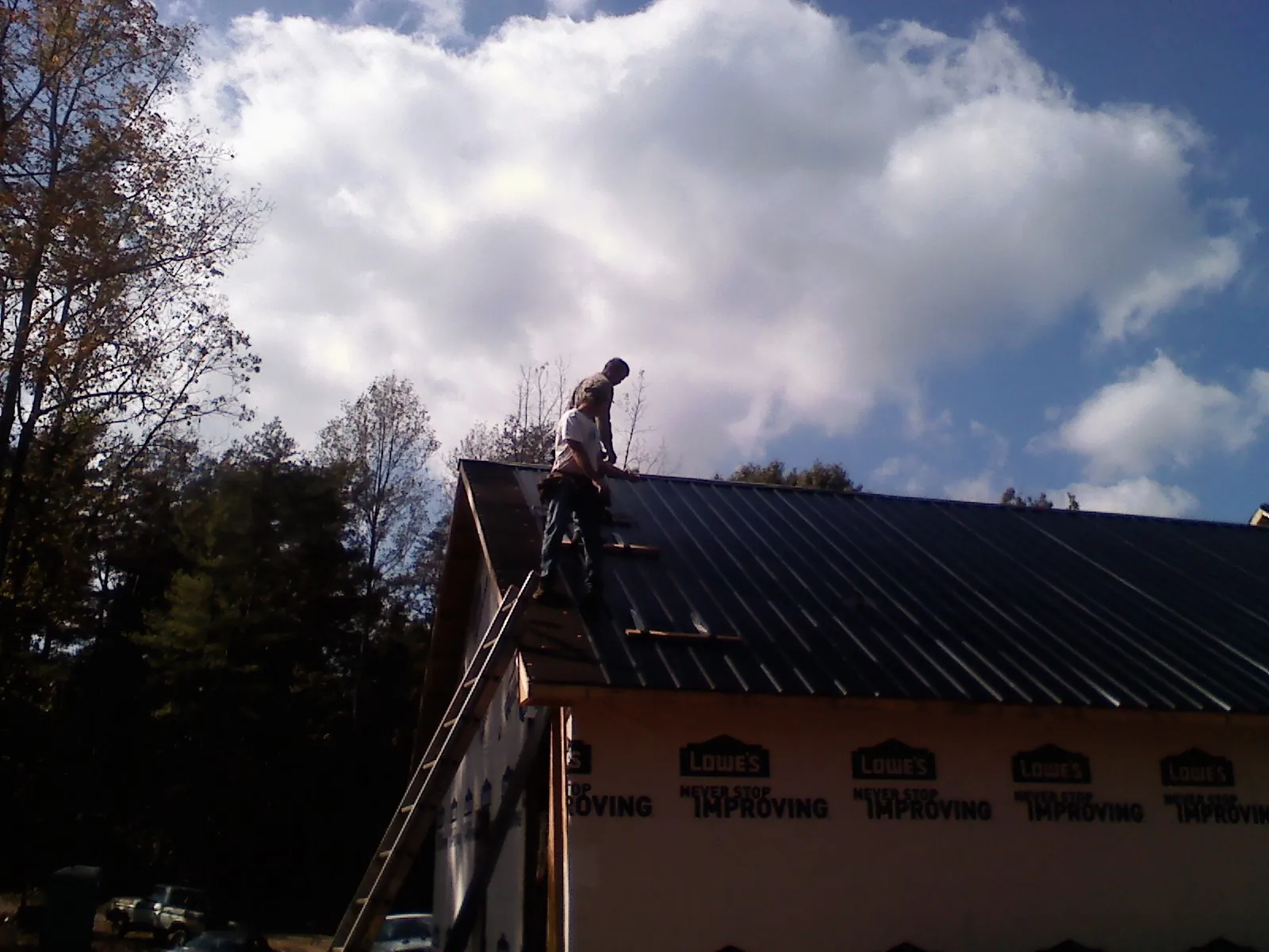 Roofer fastening dark metal panels high against a cloudy sky, from a Roof Inspection job in Beale Afb